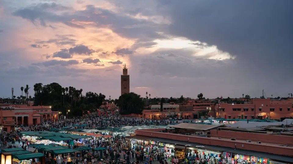 ساحة جامع الفنا في مراكش عند الغروب، بأكشاكها المضاءة وصومعة الكتبية في الأفق