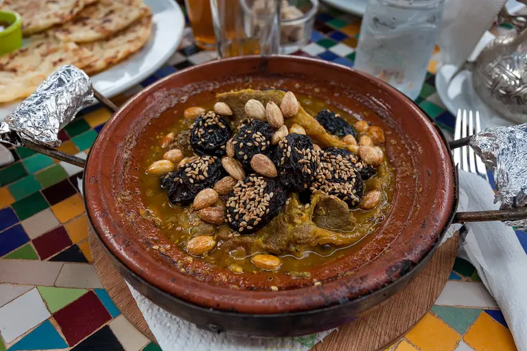 A Moroccan tajine of meat with prunes, almonds and sesame on a tiled table